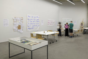 Photograph of questions hung on a wall with people looking at them