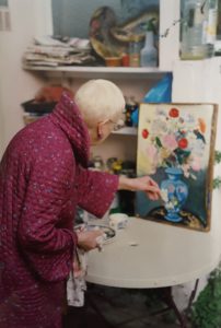The back of an older woman painting at a table
